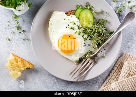 Spiegeleier mit Rucola microgreen in grauer Keramikplatte auf grauem Beton altem Hintergrund. Traditionelles englisches Frühstück. Draufsicht Stockfoto