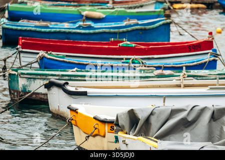 Marsaxlokk, Malta - 13. April 2025: Traditionelle, farbenfrohe maltesische Fischerboote namens Luzzu mit hellblauen, gelben und roten Details, die im malerischen Hafen von Marsaxlokk ankern Stockfoto