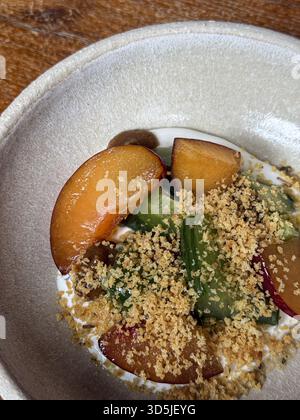 Nahaufnahme eines lebendigen Salats mit Pflaumenscheiben, Gurken, einem Streuselbelag und einem cremigen Joghurtdressing Stockfoto