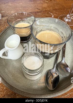 Zwei Gläser Espresso werden auf einem Tablett mit Zucker und Milch serviert Stockfoto