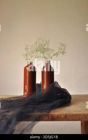 Authentische rustikale Inneneinrichtung. Holztisch, braun glasierte Tonflaschen, trockene Pflanzen, dekorativer durchscheinender Stoff, Mesh, verputzte Wände Stockfoto