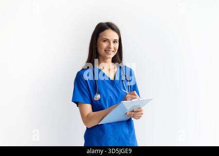 Lächelnde junge Ärztin in blauen Peelings mit Klemmbrett in den Händen Stockfoto