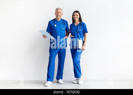 Zwei Ärzte in blauer medizinischer Uniform stehen zusammen auf weißem Atelierhintergrund Stockfoto