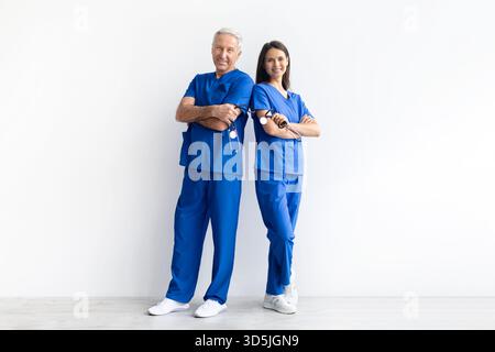 Zwei Ärzte in blauen medizinischen Peelings posieren selbstbewusst zusammen auf weißem Hintergrund Stockfoto
