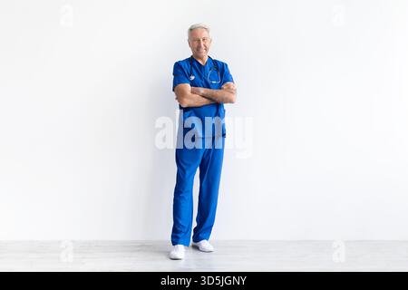 Leitender männlicher Arzt in Uniform stehend mit überkreuzten Armen auf weißem Hintergrund Stockfoto