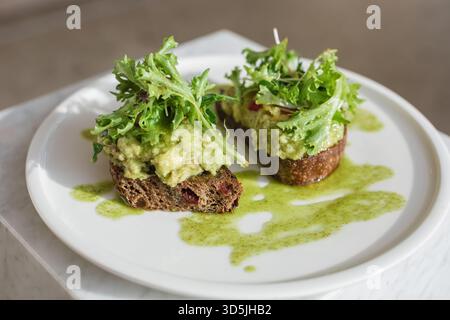Nahaufnahme von zwei Scheiben braunem Sauerteig geröstetes Brot mit Avocado und Salat auf einem Teller Stockfoto
