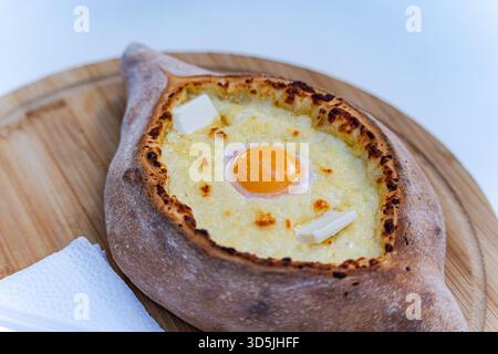 Nahaufnahme eines traditionellen georgischen Adjarianischen Khachapuri auf einem hölzernen Schneidebrett mit Papierservietten Stockfoto