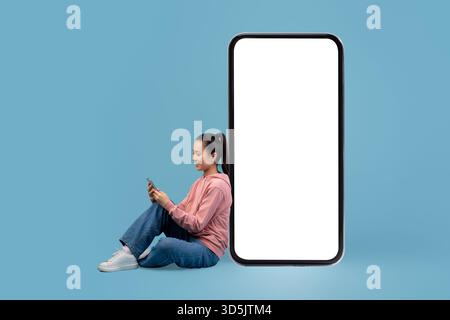 Glückliche japanische Frau, die mit einem großen Smartphone eine mobile App genießt Stockfoto