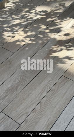 Schatten von Blättern auf einer Holzterrasse erzeugen ein natürliches Muster, ideal für Hintergrund oder Textur. Mobiles Foto Stockfoto