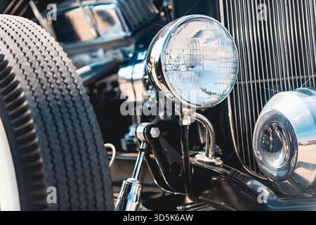 Scheinwerfer an Vintage Hot Rod mit vertikalen Gitterleisten und klassischem Reifen sichtbar. Vorderansicht mit detaillierten Fahrzeugkomponenten einschließlich m Stockfoto