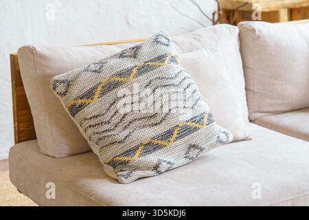 Weiches Dekokissen, Kissen mit geometrischer Webstruktur und gelbem Zickzackmuster auf hellbeigem Sofa. Gemütliches, minimalistisches skandinavisches Interieur mit Stockfoto