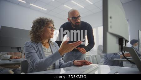 Schülerin mittleren Alters arbeitet am Computerprojekt, während die Lehrerin daneben steht und den Fortschritt anleitet und überprüft. Konzept für Erwachsenenbildung, Mentoring, digitales Lernen und berufliche Entwicklung. Stockfoto