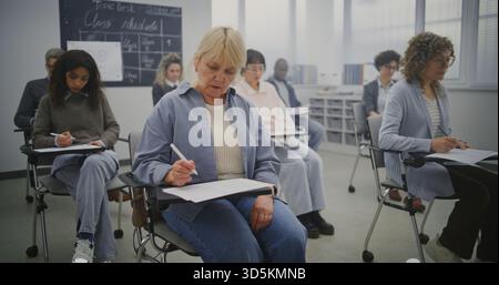 Multikulturelle Gruppe reifer Schüler, die sich während des Unterrichts im hellen Klassenzimmer Notizen machen. Schüler notieren Vorträge des Lehrers. Concept Continuing Education, Erwachsenenbildung und Wissensentwicklung. Stockfoto