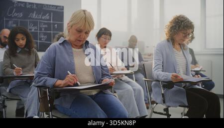 Reife multikulturelle Schüler, die an der Schulung teilnehmen, Notizen machen und dem Kursleiter zuhören. Konzept Erwachsenenbildung, Lebenslanges Lernen, Berufliches Wachstum, Modernes Bildungsumfeld. Statische Aufnahme. Stockfoto
