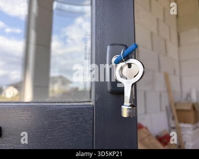 Eine Nahaufnahme von Schlüsseln, die an einem Türschloss hängen, vor einem verschwommenen Hintergrund eines privaten Neubaus. Tür- und Fensterinstallation in einem privaten Haus. Co Stockfoto