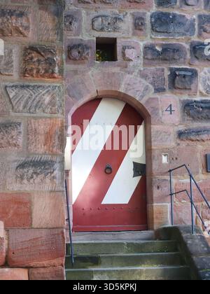 Rot-weiß gestreifte mittelalterliche Holztür in einer Steinmauer in der Altstadt von Nürnberg, Deutschland. Historische Architektur mit strukturiertem Sandstein Stockfoto