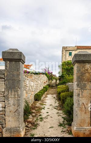 Eine ruhige ländliche Szene mit einem Kiesweg zwischen verwitterten Steinmauern, üppigem Grün und blühenden Reben. Ideal für Reisen, Tradition und Rost Stockfoto