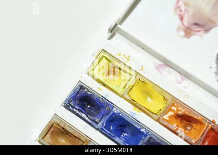 Nahaufnahme einer farbenfrohen Aquarellpalette auf weißer Oberfläche mit verspritzten Farben Stockfoto