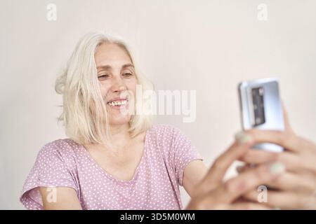 Ältere weiße Frau genießt Smartphone-Interaktion in ungezwungener Innenumgebung Stockfoto