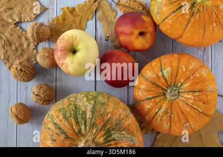 Kleine schöne Kürbisse, Walnüsse, reife Nektarinen, ein Apfel und trockene Herbstblätter sind auf einem blauen Holzhintergrund angelegt. Horizontale Ausrichtung, s Stockfoto