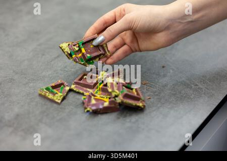 Die Hand der Frau hält ein Stück Dubai-Schokolade auf grauem Hintergrund. Grüner Kadayif und Pistazien mit Pistazien im Trenddessert. Nahaufnahme, selektiv Stockfoto