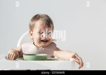 Niedliches weinendes Baby, das zu Hause im Hochstuhl sitzt, auf weißem Hintergrund, Hysterie und Tränen in einem 1 Jahr und 3 Monate alten Kind, Nahaufnahme Portr Stockfoto