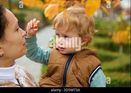 Ein zärtlicher Moment zwischen Mutter und Kleinkind draußen an einem Herbsttag, mit warmen Tönen und Blättern, die Liebe, Sorgfalt und Zweisamkeit einfangen. Stockfoto