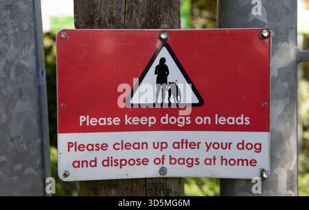 Rot-weißes Warnschild, das Hundebesitzer auffordert, Hunde an der Leine zu halten und nach ihren Haustieren in einem öffentlichen Bereich zu säubern Stockfoto