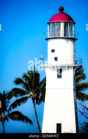 Weißer und roter Leuchtturm an der Küste von Ohau, Hawaii unter einem klaren blauen Himmel mit Palmen im Hintergrund. Stockfoto