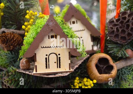 Ein bezauberndes hölzernes Miniaturhaus hängt an einem Weihnachtsbaum. Weihnachtsdekoration Stockfoto