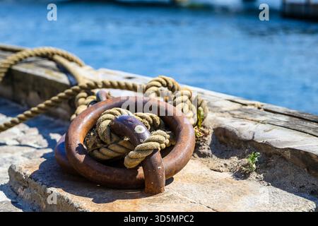 Seil um einen Metallanlegerring an einem Kopenhagener Kai gebunden, mit blauem Hafenwasser im Hintergrund. Stockfoto
