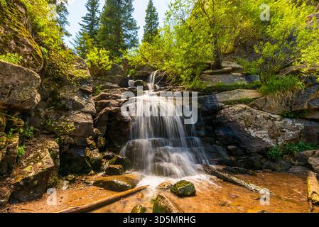 Ruhiger Waldwasserfall, der über Moosfelsen in einer sonnendurchfluteten Bergschlucht fällt Stockfoto