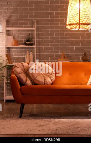 Inneneinrichtung des modernen Wohnzimmers mit rotem Sofa, Kissen, Regalfach und leuchtender Lampe am Abend Stockfoto