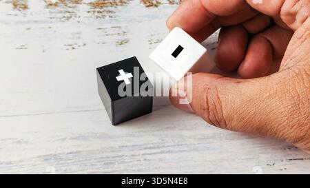 Hand halten Schwarzweiß-Würfel mit Plus- und Minuszeichen, die für Vergleich, Pro, Contra und Entscheidungsfindung stehen Stockfoto
