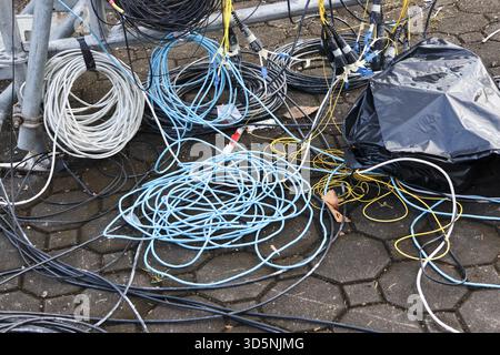 Unordentlicher Haufen von verworrenen elektrischen Drähten und Kabeln auf der Erde im Freien. Chaotischer Industriehintergrund mit buntem Kabel und Verbindungstest Stockfoto
