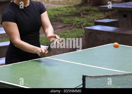 Konzentrierte Frau im aktiven Spiel während eines Tischtennisspiels im Freien. Lustiges Hobby für Freizeitaktivitäten im Park, hält sie ihr Paddel für den nächsten Schuss bereit Stockfoto