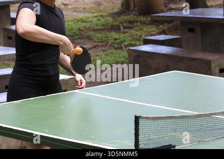 Fokussierte Frau, die ein aktives Tischtennis-Spiel im Park spielt. Freizeitsport mit Paddel, Ball und Netz für Spaß, Wettkampf-Freizeit-AC Stockfoto