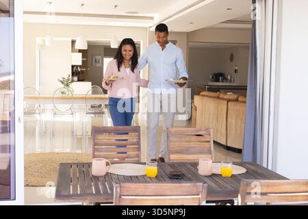 Glückliches Paar, das Frühstücksteller zu Hause auf der Terrasse trägt Stockfoto