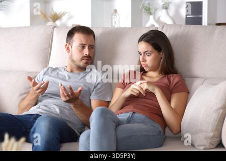 Eine verblüffte Frau, die zuhört, wie ihr Partner zu Hause auf einer Couch sitzt Stockfoto