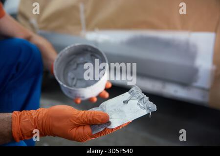 Die Nahaufnahme eines Technikers bereitet in einer Werkstatt eine Fahrzeugplatte mit Grundierung sorgfältig vor Stockfoto