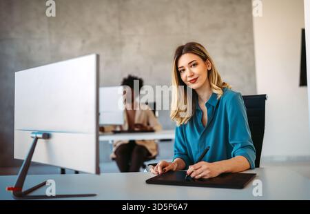 Junge erfolgreiche Geschäftsfrau, die einen Computer benutzt, während sie in einem Startup-Büro arbeitet Stockfoto