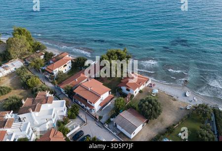 Ein wunderschöner Strand mit Häusern und einer kleinen Stadt im Hintergrund. Die Häuser sind weiß und rot, und das Meer ist blau Stockfoto