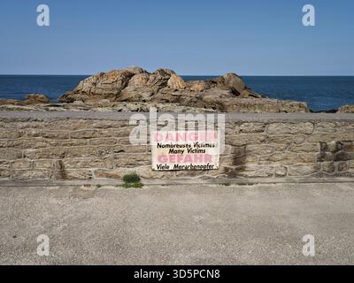 Warnschild an einer niedrigen Steinmauer vor Erosion geformten Felsformationen, Saint Guenole, Bretagne, Frankreich. Stockfoto