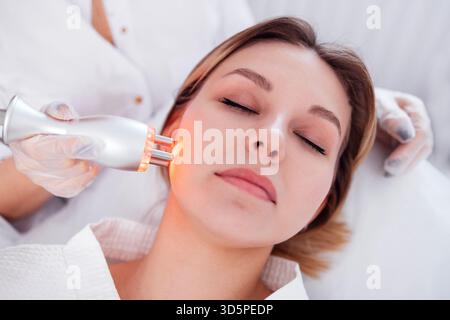 RF-Gesichtskavitation-Lifting-Verfahren in einem Schönheitssalon. Frau, die sich einer Gesichtsbehandlung mit innovativem Hautpflegegerät in ruhiger Spa-Umgebung unterzieht, hig Stockfoto
