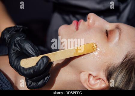 In einem Schönheitssalon wendet der Ästhetiker eine Gesichtsbehandlung mit Holzspachtel auf die Haut des Kunden an und hebt dabei die Techniken der Hautpflege und die ruhige Atmosphäre hervor Stockfoto