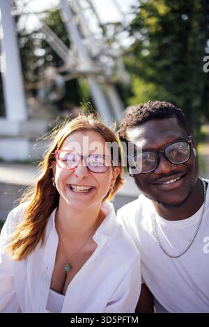 Glückliche Frau und Mann, die eine Brille tragen, genießen einen sonnigen Tag im Freien, umgeben von üppigem Grün und Vergnügungsfahrten, um einen Moment der Freundlichkeit festzuhalten Stockfoto
