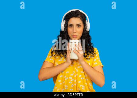 Eine junge Frau, die auf einem Reisebecher bläst, während sie Musik hört Stockfoto