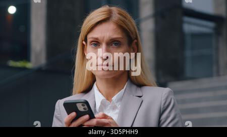 Ernsthaft verärgert kaukasische Geschäftsfrau mit Handyversagen traurige Geschäftsfrau mittleren Alters Frau mit Smartphone in der Stadt frustriert anzusehen Stockfoto