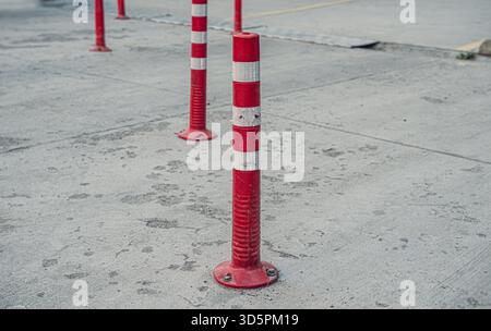 Aus nächster Nähe rot-weiß gestreifte Verkehrsbarrieren, die auf einer Betonoberfläche stehen und deren Design und die Umgebung hervorheben. Stockfoto
