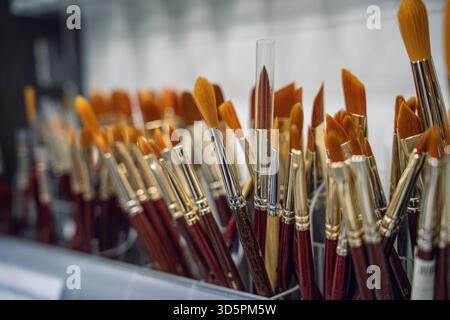 Aus nächster Nähe sehen Sie eine vielfältige Sammlung von Farbpinseln, die in einem Behälter angeordnet sind und ihre leuchtenden Borsten und metallischen Ferrules zeigen. Stockfoto